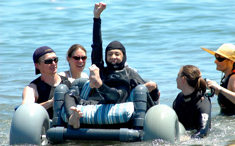 Volunteers help a disabled person to ride a watercraft in the ocean.