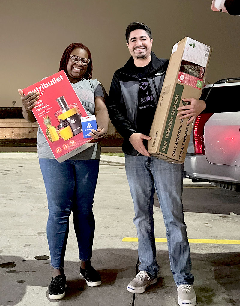 Man and woman standing in a parking lot, holding Christmas gifts and a Christmas tree
