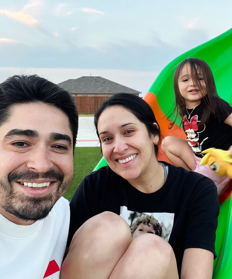 A smiling man, woman, and child playing on a slide at a park