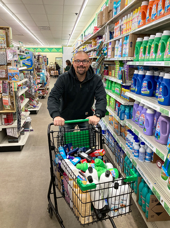 Image: A man pushing a shopping cart full of shampoo, conditioner, laundry soap, and other items. CharityRx 12 Days of Hope. 