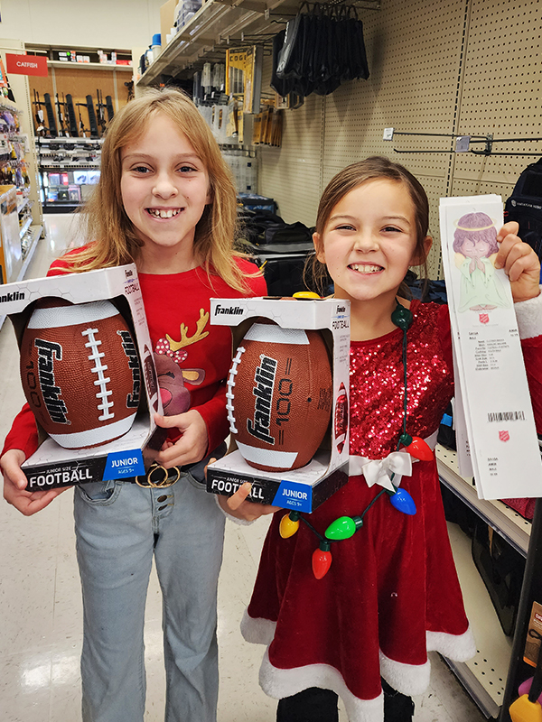 Image: Two young, smiling girls hold footballs and cards from the Salvation Army Angel Tree. CharityRx 12 Days of Hope.  