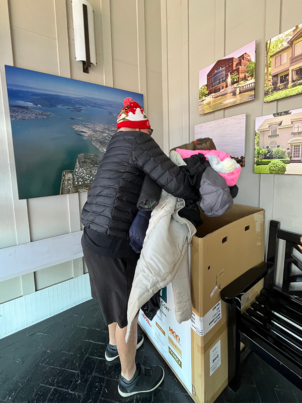 Image: A man donating an armful of winter coats and placing them in the donation box. CharityRx 12 Days of Hope. 