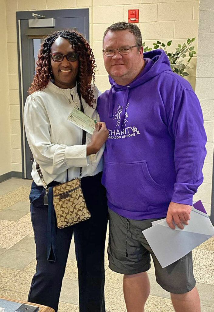 CharityRx cares about kids school lunch debt. David Beckley wearing a purple CharityRx hoodie standing next to administrator at James Island Elementary School who is holding a check.