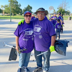 Ray Rios and his wife, Norma Rios, standing together outside in purple Beautify Fresno t-shirts. They are holding gloves, trash bags, and trash picking tools. CharityRx Reps Serve Nationwide on Founder’s Day