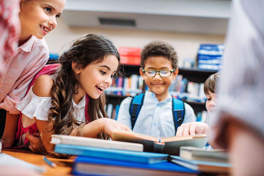 CharityRx Charity of the Month Helps Kids. Group of kids in a school library, leaning over a table covered with stacks of books