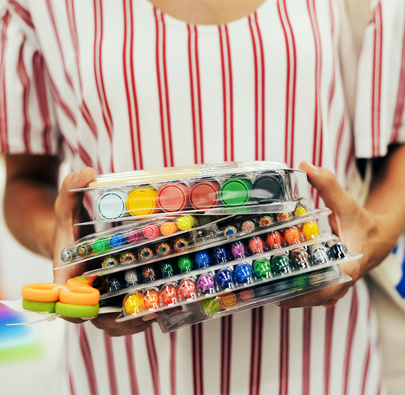 CharityRx Charity of the Month Helps Kids. Woman in a red and white striped dress, holding a stack of school supplies