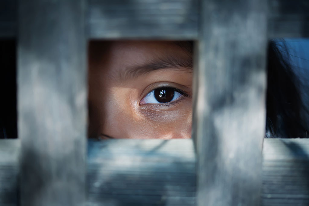CharityRx partners with Operation Underground Railroad (O.U.R). A child looks out through a grid of bars. Only their eye and part of their face are visible.
