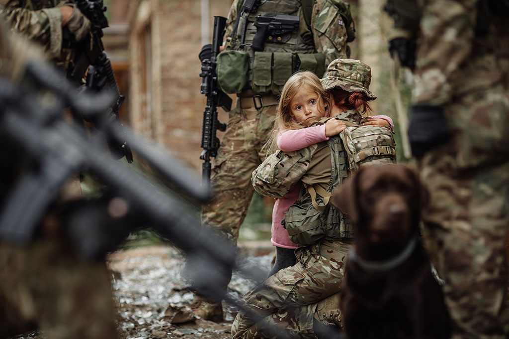 CharityRx partners with Operation Underground Railroad (O.U.R). A group of soldiers in camouflage combat gear surround a young girl in a pink dress hugs a female soldier who has bent down to her knees.