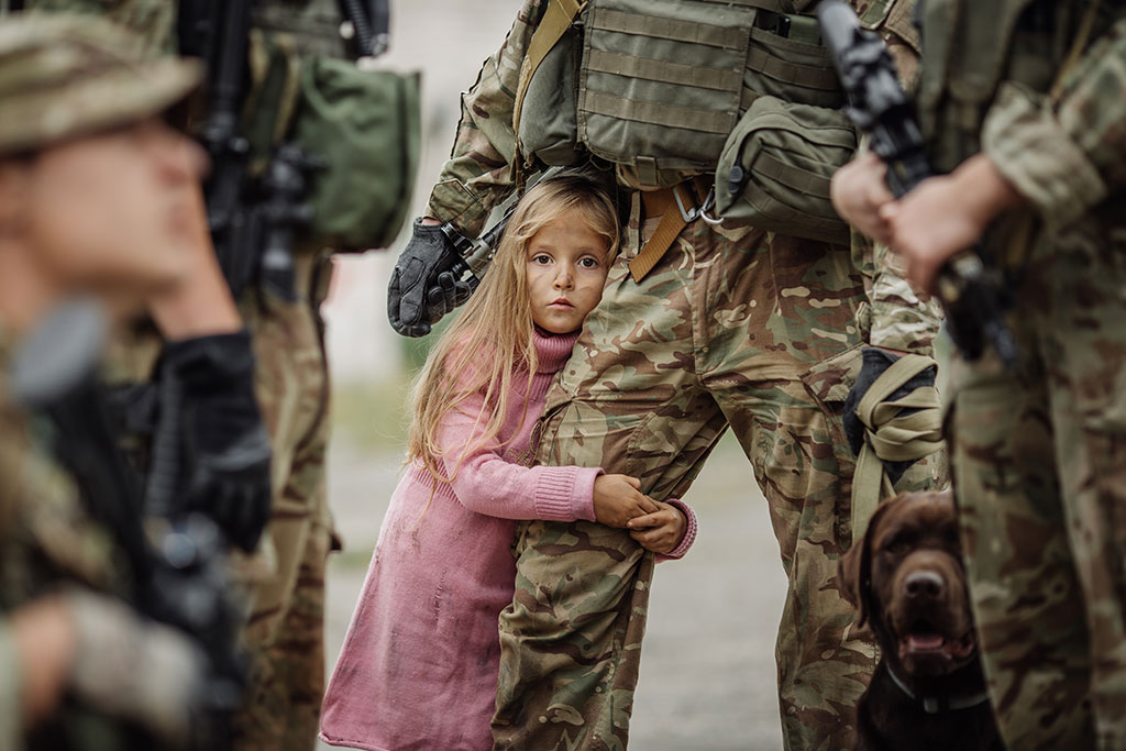 CharityRx partners with Operation Underground Railroad (O.U.R). A small girl in a pink dress hugs the leg of a soldier wearing camouflage combat gear.
