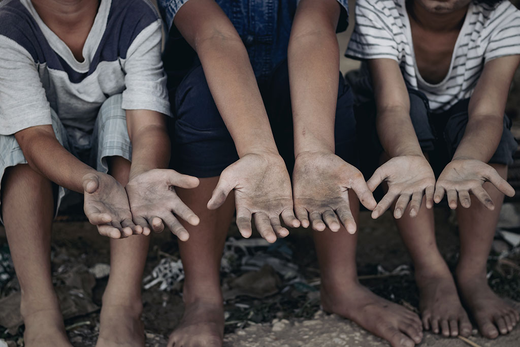 Image of three very dirty and barefoot children, sitting in the dirt, holding their hands up for donations.
