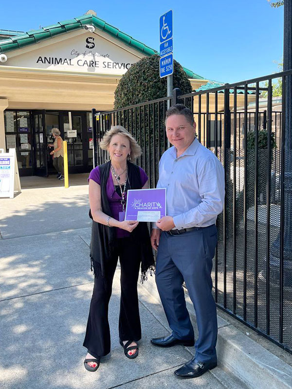 CharityRx Reps Rescue Shelter Pets with Donations. A woman and man stand together outside the Front Street Animal Shelter. They are smiling and holding a check between them.