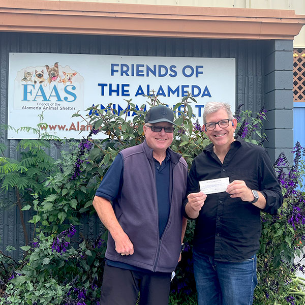 CharityRx Reps Rescue Shelter Pets with Donations. Two middle-aged men stand smiling in front of the Friends of the Alameda Animal Shelter facility. The man on the right is holding a check.