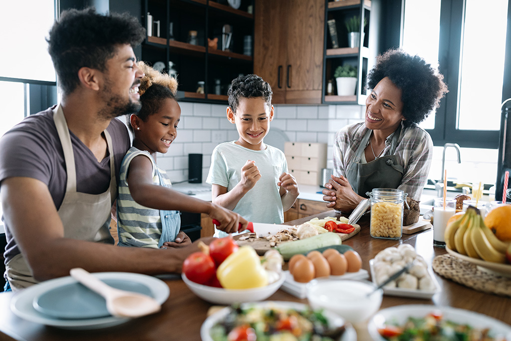 CharityRx helping to reduce food insecurity in America with Feeding Youth USA. Happy young Black family with mother, father, son, and daughter cooking healthy food at home