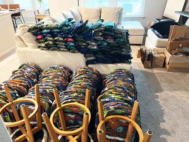 Image: School supplies and backpacks arranged on a sofa and table in a living room.