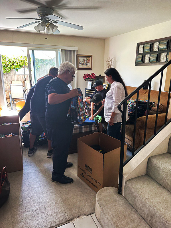 Image: Several people stand in a living room amidst cardboard boxes and school supplies.