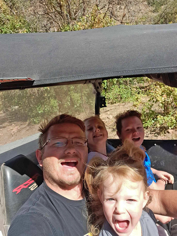 Meet CharityRx Rep David Gingrass. Image: David with three young children smiling and riding in a UTV in the mountains.