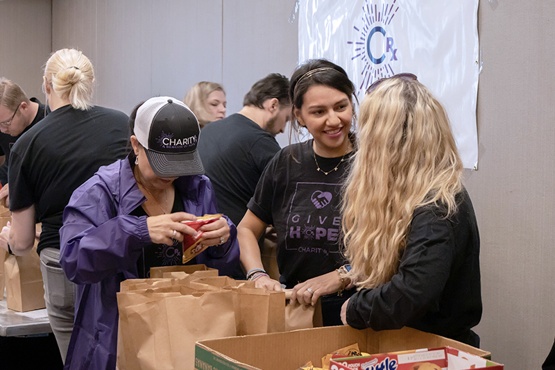 CharityRx Founder's Day 2023: The Power of Giving Back. Image: Three women stand around a table, checking that each bag has the correct items inside.