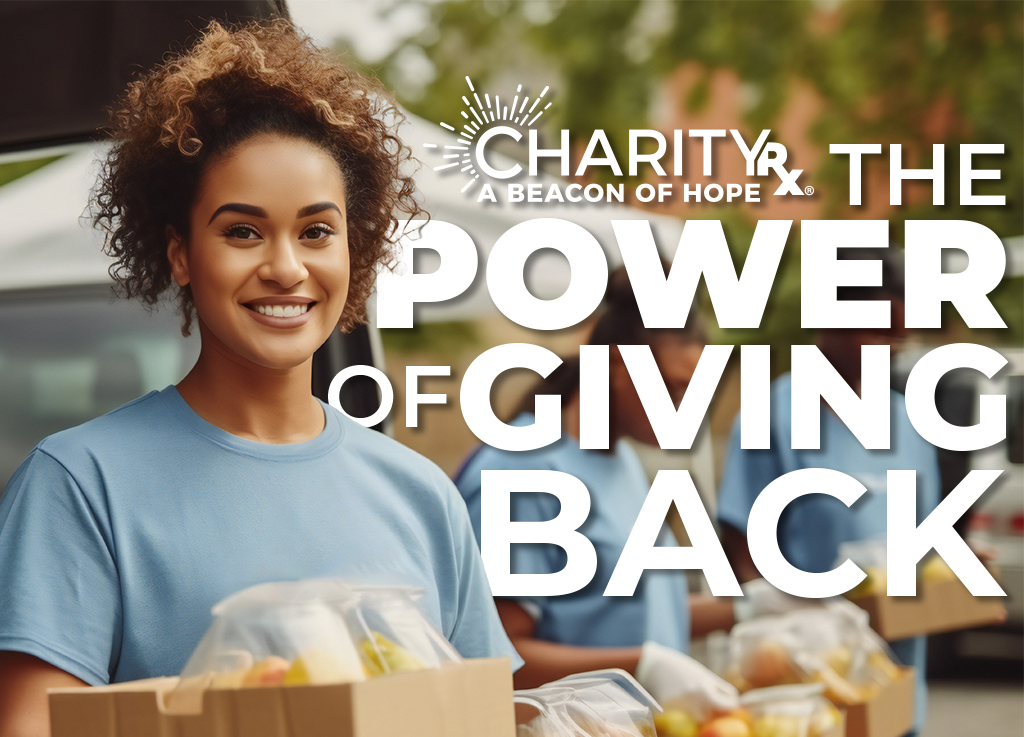 CharityRx Founder's Day 2023: The Power of Giving Back. Image of a bipoc woman, smiling and standing outside behind boxes of food. 