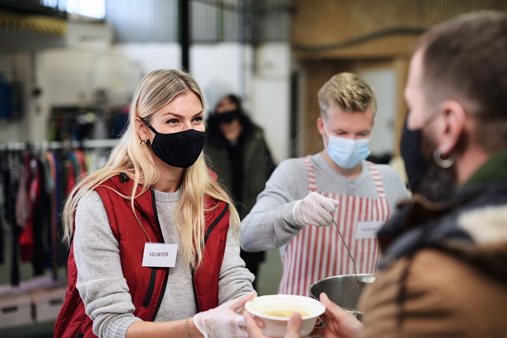 CharityRx Food Foundation donating meals for Thanksgiving. A young, blonde woman volunteer hands a bowl of soup to a man. A young male volunteer stands next to her ladling soup out of a large stock pot.