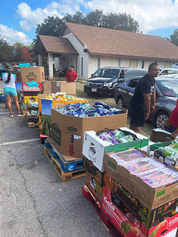 CharityRx Founder's Day 2023: The Power of Giving Back. Image: Several people stand in a parking lot between large boxes of food.