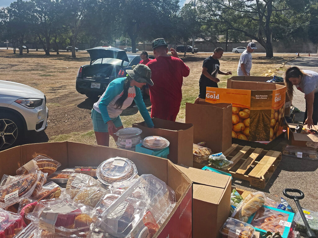 CharityRx Founder's Day 2023: The Power of Giving Back. Image: A group of people are working to organize food into large boxes outside at a local park.
