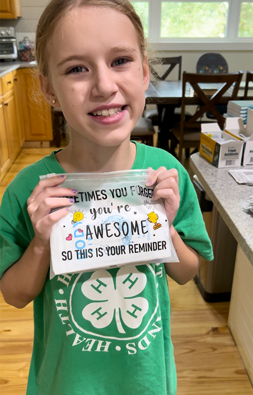 CharityRx Founder's Day 2023: The Power of Giving Back. Image: A smiling, young, blond girl holds a pencil pouch in front of her that reads "Sometimes you forget you're awesome so this is your reminder."