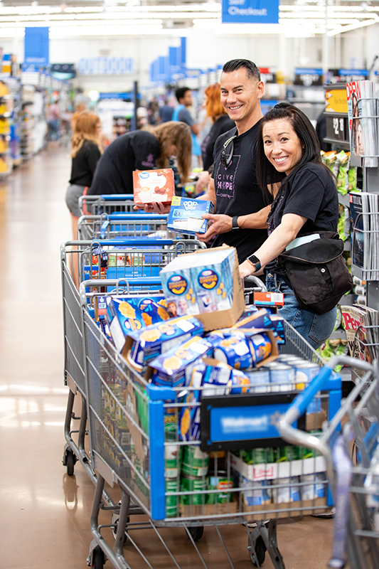 CharityRx Food Foundation donating meals for Thanksgiving. A smiling man and woman stand in a grocery store behind four shopping carts filled with food.