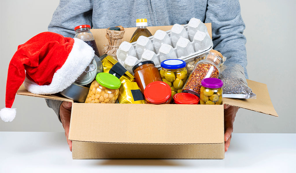 Image: A large box of food for donation with a Santa hat over one corner. CharityRx 12 Days of Hope. 