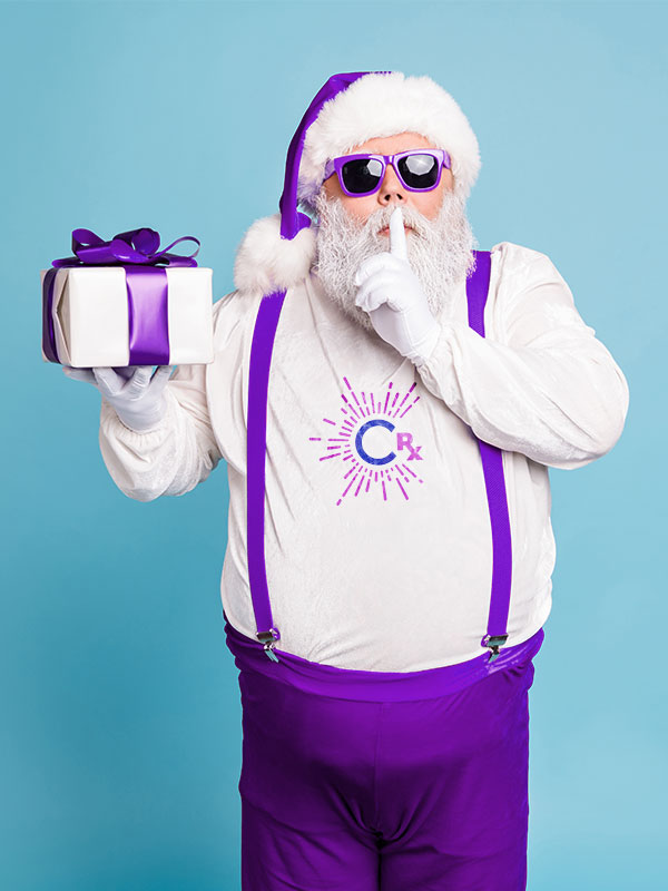 Image: Santa stands with a finger to his lips as in Shhhh... He is dressed in purple holding a package wrapped in white with purple ribbon. CharityRx 12 Days of Hope. 
