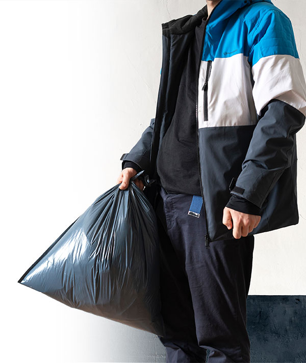 January 2024 Charity of the Month: Foster Hope. Image: A young boy wearing black clothes and a blue, white, and black striped coat holds a black plastic garbage bag in one hand.