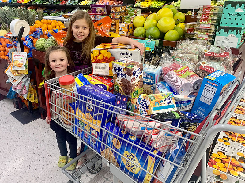 Image of two smiling young girls standing next to a cart full of food.