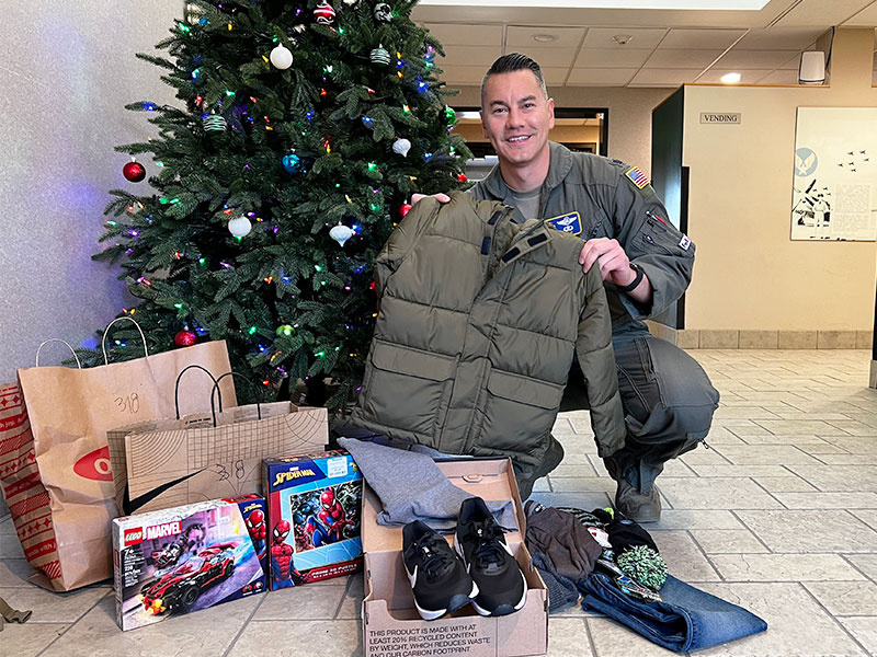 Image of a man kneeling in front of a Christmas tree next to several bags and boxes of gifts.