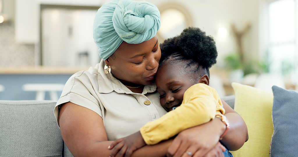 Image of a happy black mother and daughter snuggling on a sofa. 