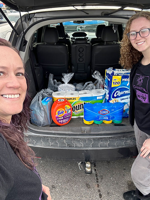 Image of two smiling women standing next to a car full of household items to be donated.  CharityRx Spreading Hope Through Donations