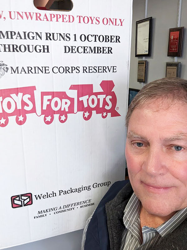 Image of a middle-aged man standing in front of a Toys For Tots donation box. CharityRx: Spreading Hope Through Donations