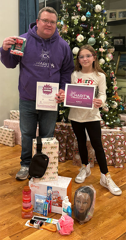 Image of a middle-aged man and young girl standing in front of a Christmas tree with gifts at their feet. CharityRx Spreading Hope Through Donations