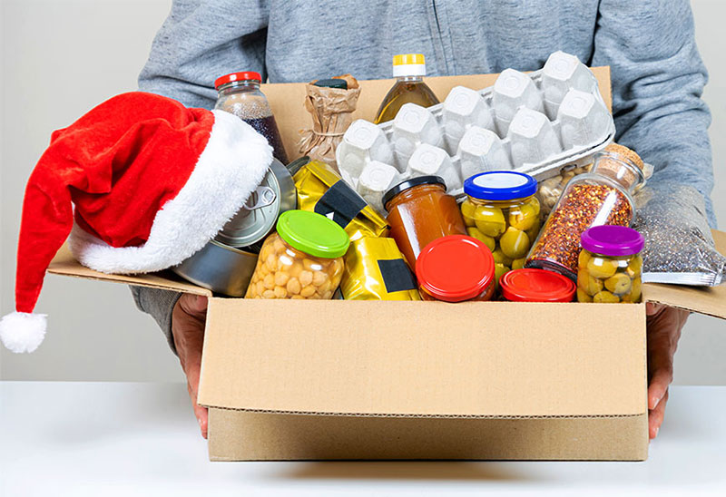A cardboard box of food to donate with a Santa hat placed on top