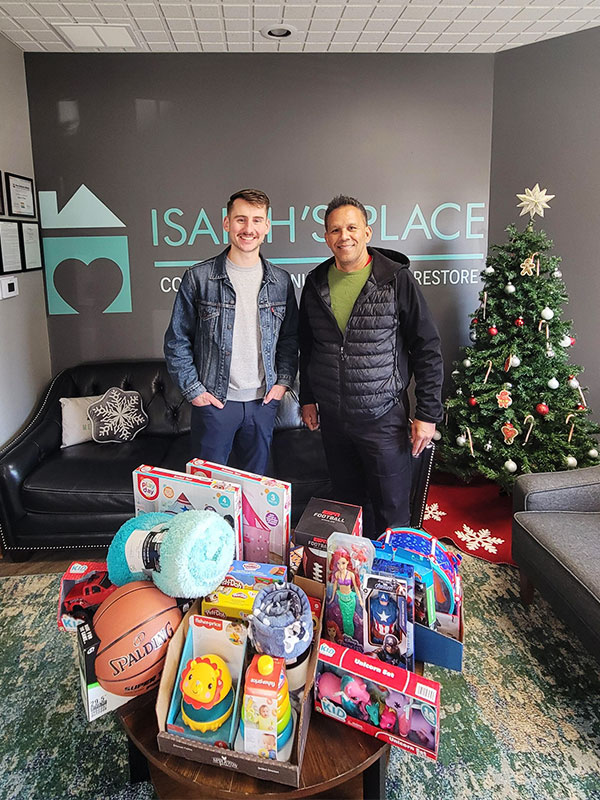Image of two men standing in the lobby of Isaiah's Place with a pile of toys and gifts in front of them. CharityRx: Spreading Hope Through Donations