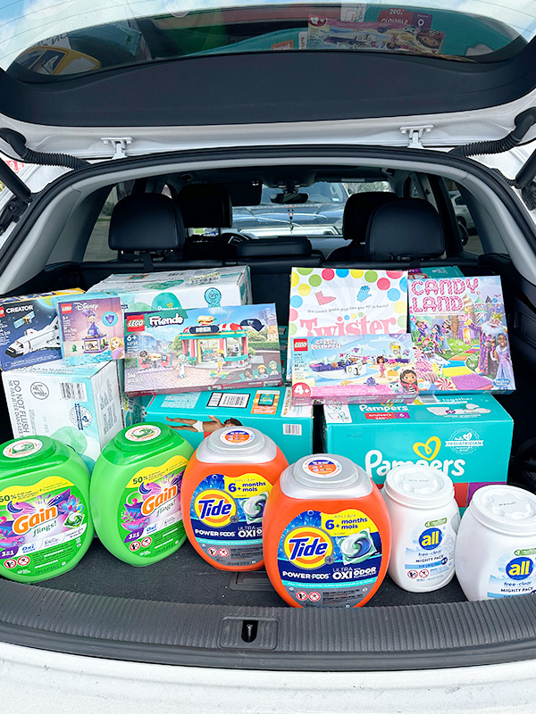 Image of the back of a vehicle with the hatch open and filled with diapers, laundry soap, and board games to be donated to Safe Alliance. CharityRx Supports Women and Children