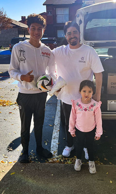 Image of a man, teenage boy holding soccer cleats and a ball, and young girl standing outside next to a vehicle, smiling with thumbs up. CharityRx Spreading Hope Through Donations