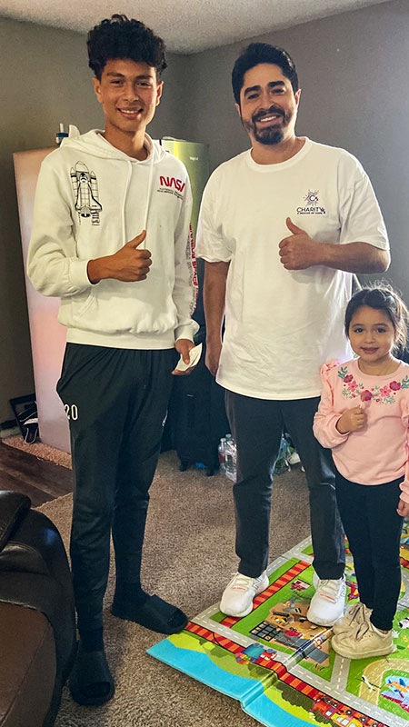 Image of a man, teenage boy, and young girl standing inside a house smiling with thumbs up.