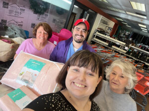 Image of three middle-aged women and one man, all smiling as they accept a donation of blankets. CharityRx Supports Women and Children