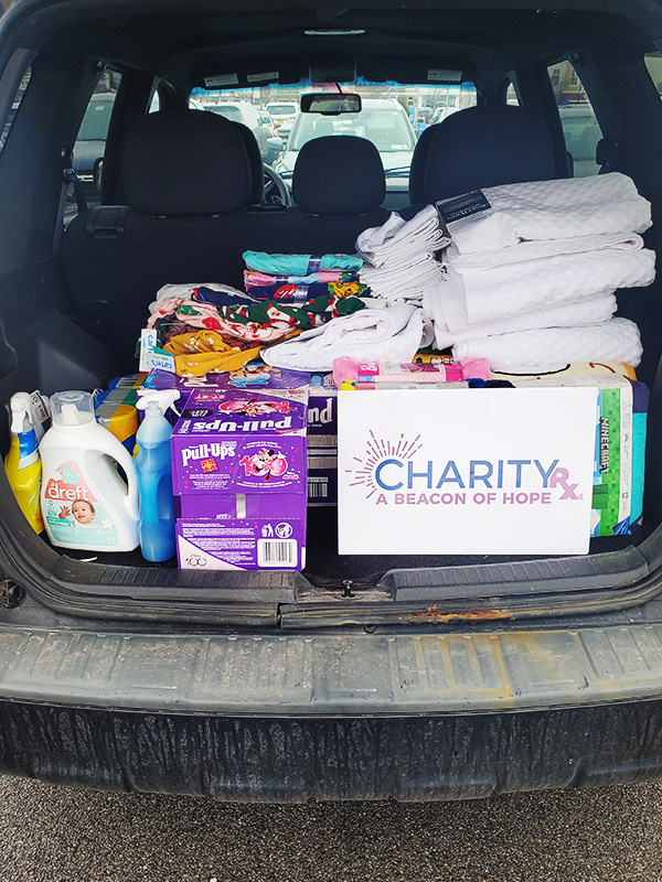 Image showing the back of a vehicle with the hatch open and stacks of diapers, cleaning supplies, clothing and other household items to be donated. CharityRx Supports Women and Children