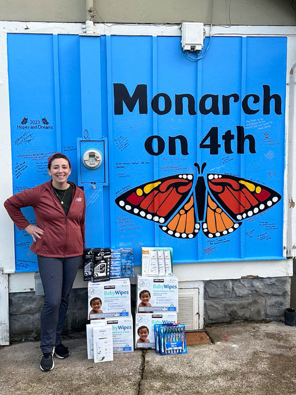 Image of a woman standing outside Monarch on 4th next to stacks of baby wipes and other hygiene items.