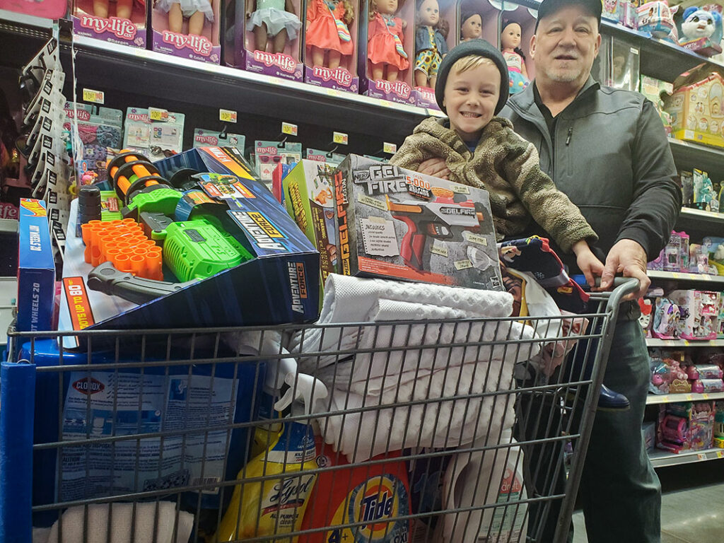 Image of an older man pushing a young boy in a shopping cart full of toys and household products. CharityRx Spreading Hope Through Donations