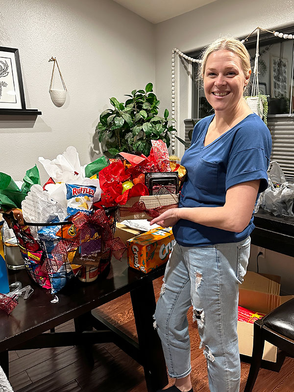 Image of a smiling woman next to a table full of gift baskets with snacks and drinks.