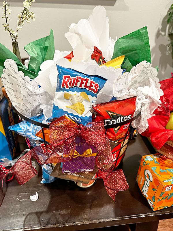 Image of a gift basket with white paper, full of chips, snacks, and gift cards.