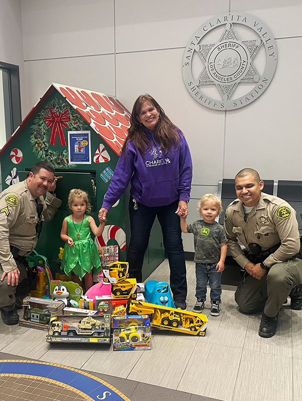 Image of a woman, two police officers, and two young children next to a stack of donated toys. CharityRx Spreading Hope Through Donations