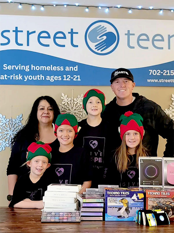 Image of a smiling man, woman, and four children standing behind a stack of gifts and in front of a Street Teens sign. CharityRx Spreading Hope Through Donations