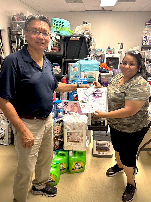 Image of a man and woman standing inside a storage room next to donated household and personal care items. CharityRx Supports Women and Children